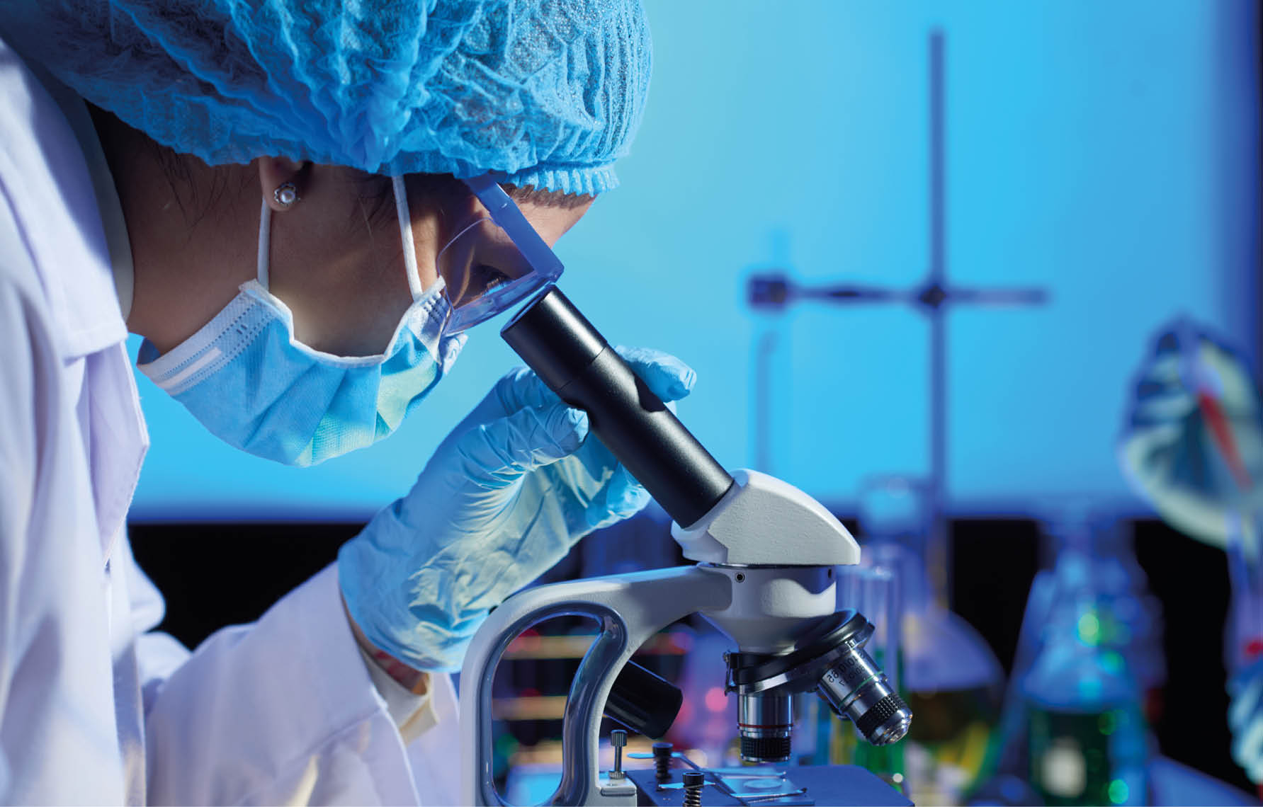 Profile view of concentrated Asian microbiologist examining sample with help of modern microscope while wrapped up in work at dim laboratory