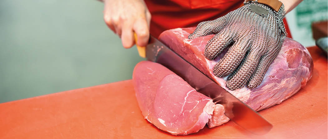 Female butcher cutting fresh meat in a butcher shop with metal safety mesh glove 