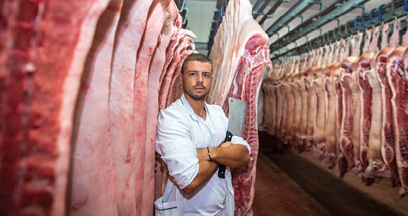 Portrait of young butcher holding chopper knife in meat processing industry 