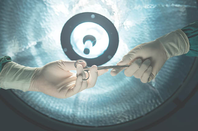 healthcare and medical concept   Close-up of surgeons hands holding surgical scissors and passing surgical equipment on background of surgical lamp