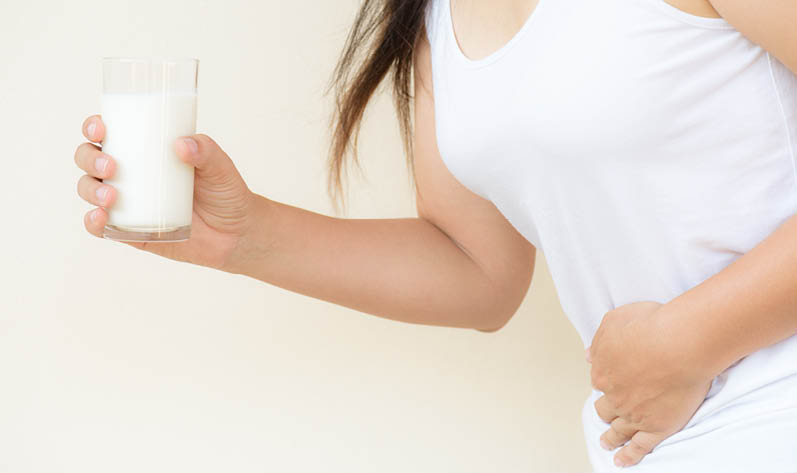 Woman hand holding glass of milk having bad stomach ache because of Lactose intolerance  health problem with dairy food products  Healthcare and medical concept 