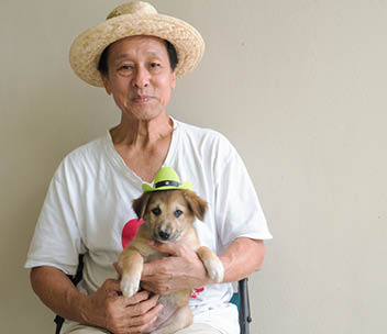 Retired male senior is sitting on chair holding little puppy dog on his lap with happiness as healthy lifestyle concept