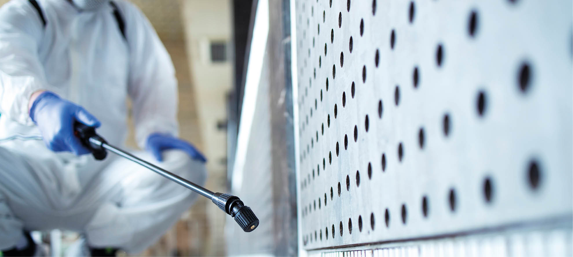 Unrecognizable person in white chemical protection suit doing disinfection of public areas to stop spreading highly contagious corona virus 