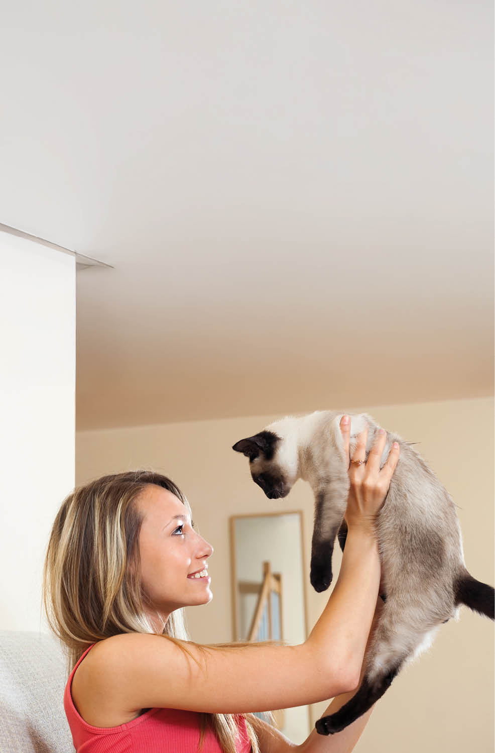 Cute girl playing with Siamese kitten on couch at home