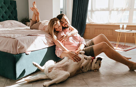 Guy and his girlfriend are resting in bedroom  Happy couple lovingly looking at their pet who wants to play
