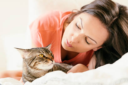 Happy woman kissing her cat in bedroom  Focus on cat