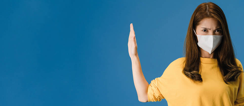 Young Asia girl wear face mask doing stop sing with palm of hand with negative expression and looking at camera  Social distancing, quarantine for corona virus  Panoramic banner blue background 